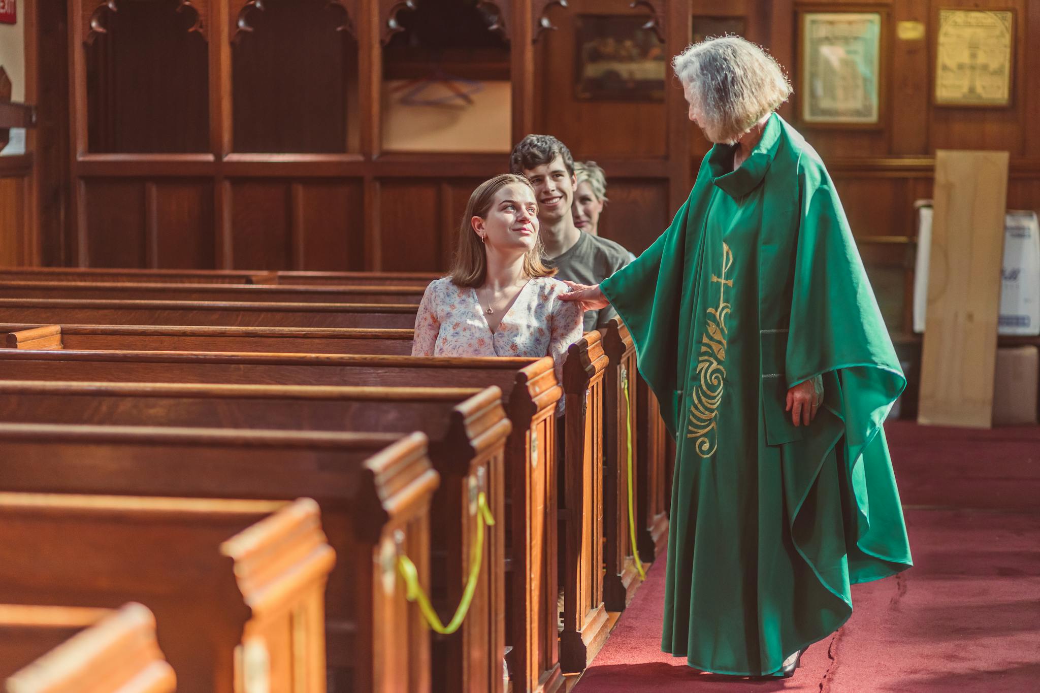 Clergy member greets young adults inside a traditional church setting.